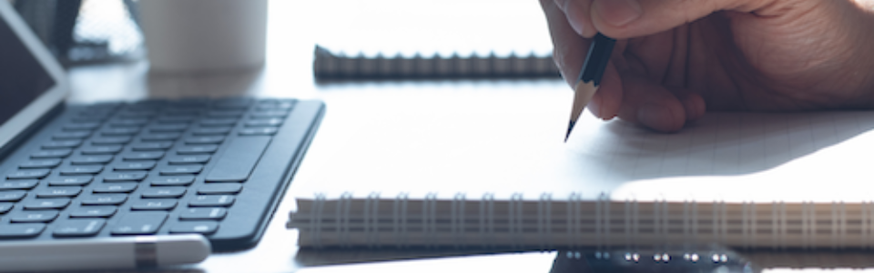 A man writing on paper in front of a laptop